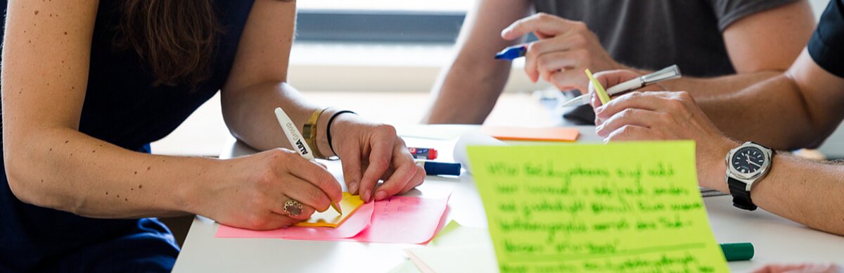 verschiedene Hände gestikulierend mit Post-its und Stiften am Tisch